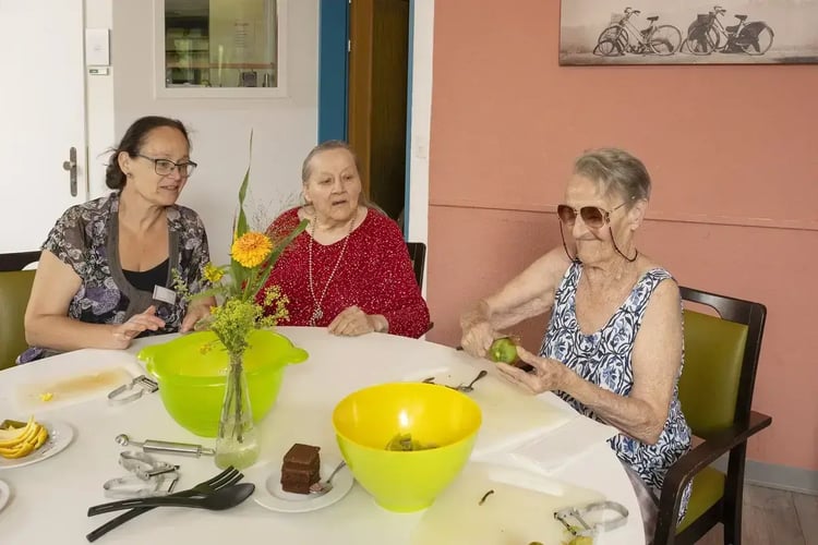 Drei Seniorinnen schneiden gemeinsam Gemüse am Tisch