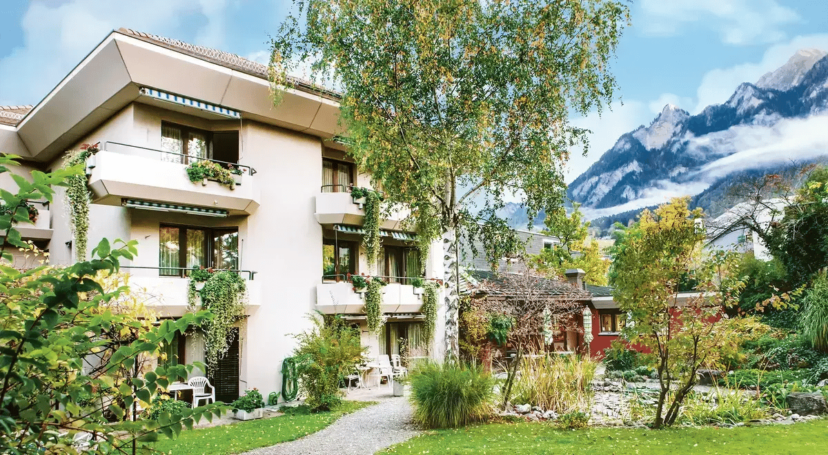 Das Tertianum Villa Sarona Gebäude in einem grünen Garten mit Blick auf die Berge