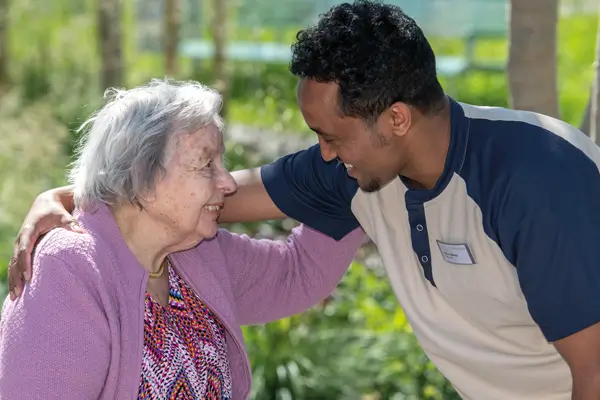 Ein Tertianum-Mitarbeiter umarmt eine ältere Dame und sie lachen und unterhalten sich an der frischen Luft